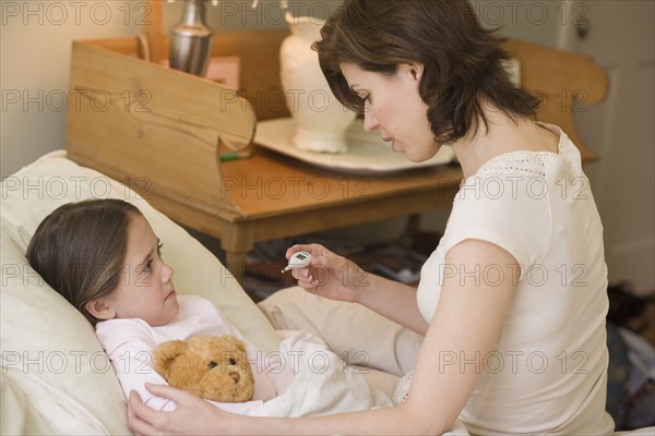 Mother checking young daughter’s temperature with thermometer.