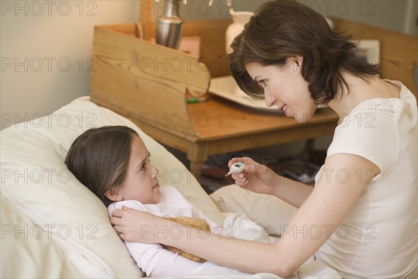 Mother checking young daughter’s temperature with thermometer.