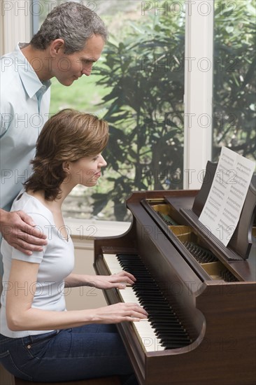 Woman playing piano with man watching.