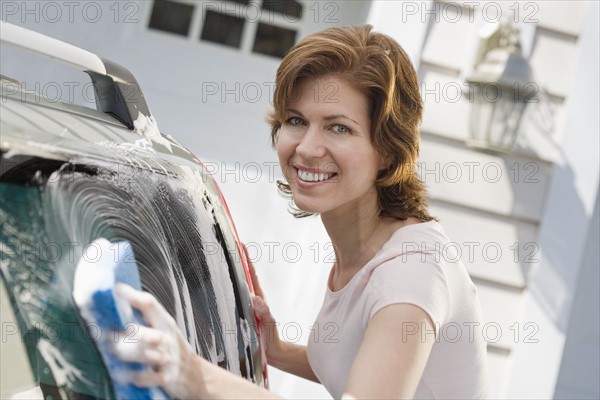 Woman washing car in driveway.