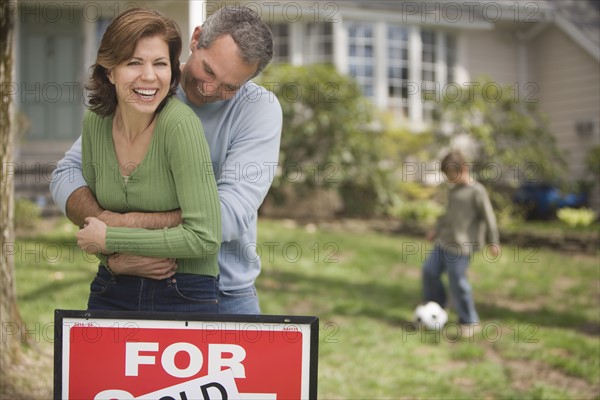 Family in front of house with For Sale/Sold sign.