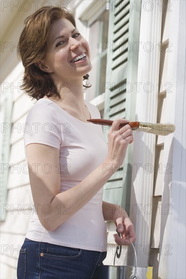 Woman painting exterior of house.