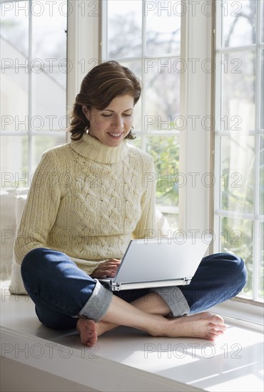 Woman sitting in window alcove with laptop.