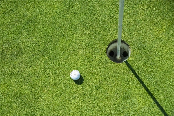 Golf ball near cup on putting green outdoors.