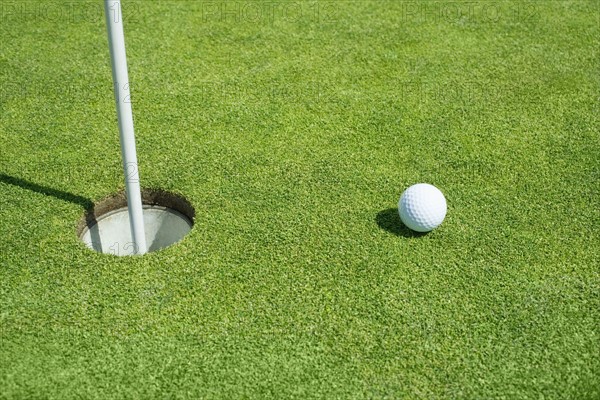 Golf ball near cup on putting green outdoors.