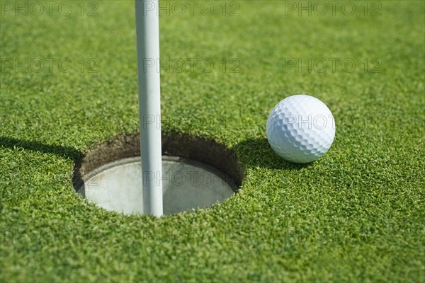 Golf ball near cup on putting green outdoors.