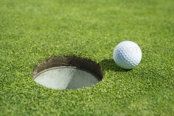 Golf ball near cup on putting green outdoors.