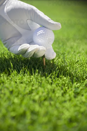 Gloved hand placing golf ball and tee into turf.