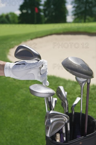 Hand selecting golf club with course in distance.