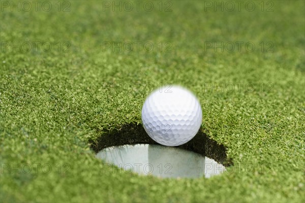 Golf ball dropping into hole on green.