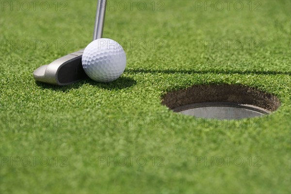 Closeup of golf ball and club near cup.