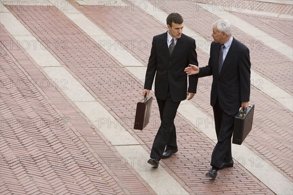 Two business men walk and talk outdoors.