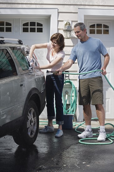 Couple washing car in driveway.