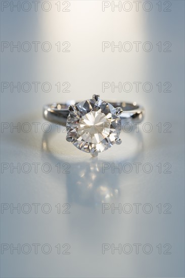 Diamond like ring in six pronged silver setting on table.
