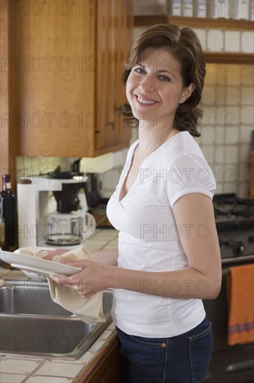 Woman drying dish at kitchen sink.
