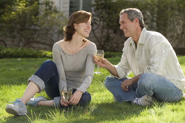 Couple sitting in grass drinking wine.