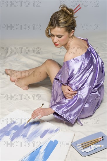 Woman in purple kimono with paint and brushes.