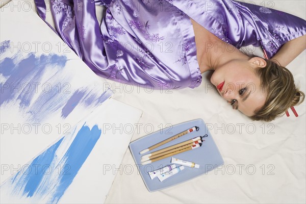 Woman in purple kimono with paint and brushes.