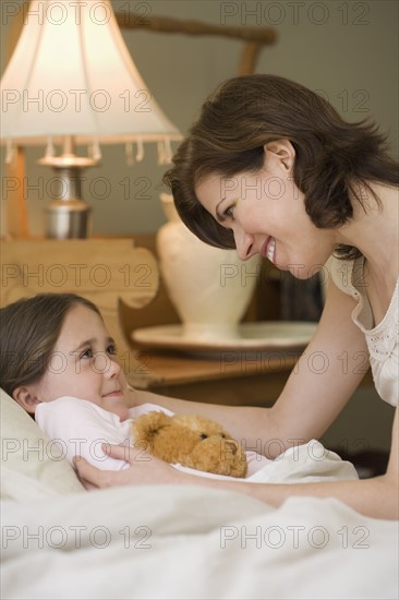 Mother tucking young daughter into bed.