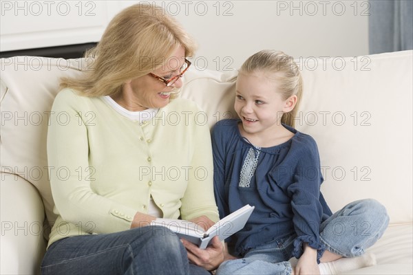 Grandmother reading to young granddaughter on sofa.