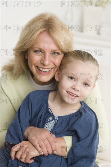 Grandmother and young granddaughter hugging sofa.