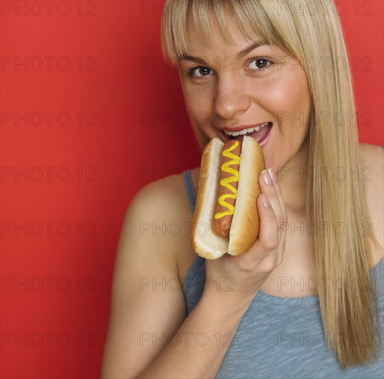 Studio shot of woman eating hot dog with mustard.