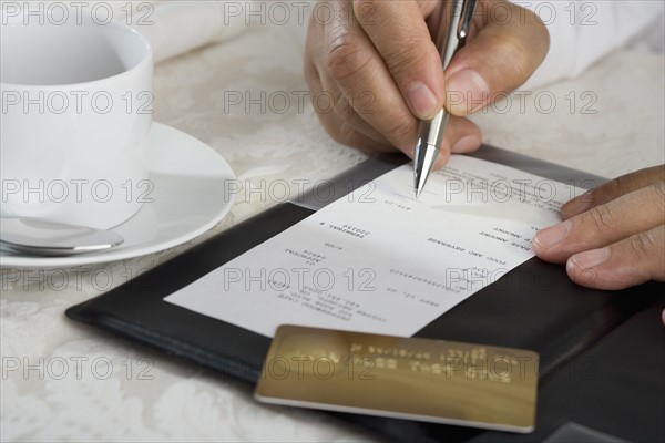 Close up of man signing credit card receipt at restaurant.