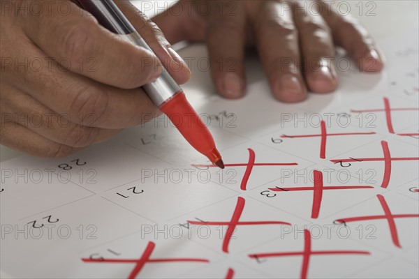 Close up of man crossing out days on calendar.