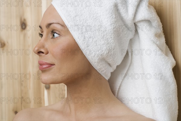 Woman in sauna with head wrapped in towel.