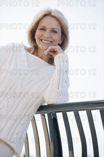 Senior woman leaning on railing outdoors.