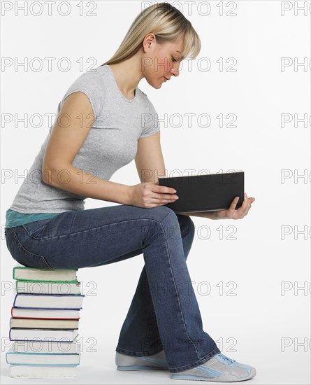 Studio shot of woman sitting on stack of books reading.