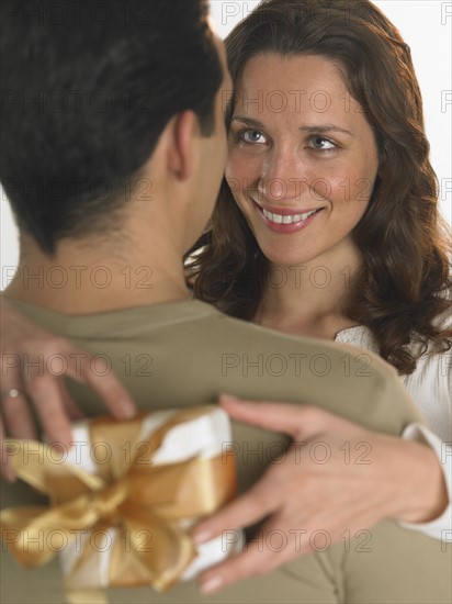 Woman holding gift with arms around man.