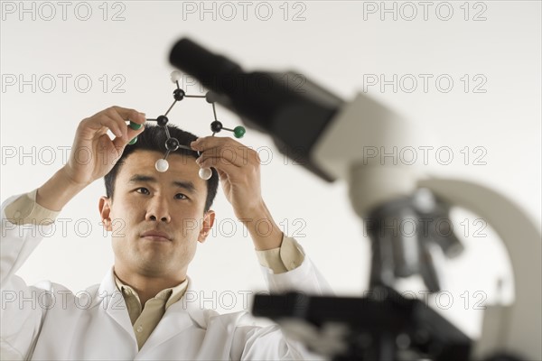 Scientist with microscope holding molecular model.