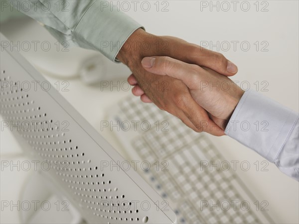 Two men shaking hands over computer.
