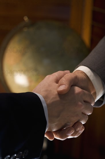 Two men shaking hands with globe in background.