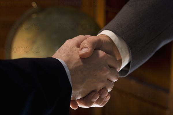 Two men shaking hands with globe in background.