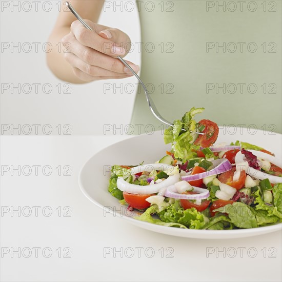Close up of woman eating plate of salad.