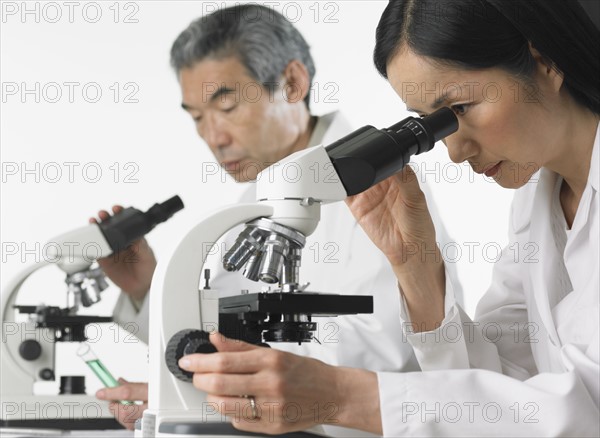 Man and woman in lab coats using microscopes.