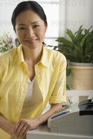 Asian woman smiling and leaning on cash register.