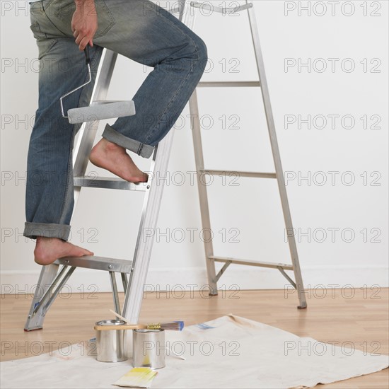 Man walking up ladder with paint roller indoors .