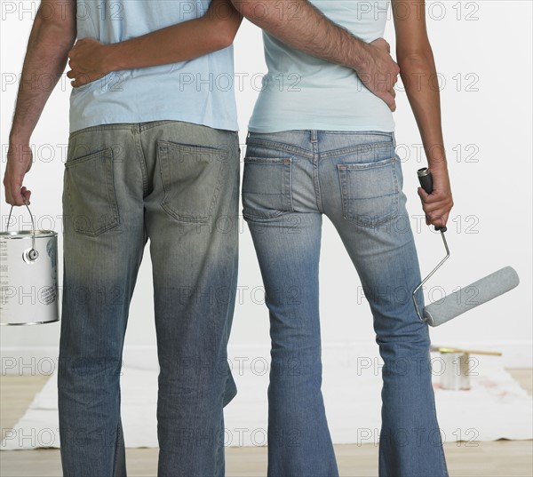 Rear view of couple with paint roller and paint can indoors.