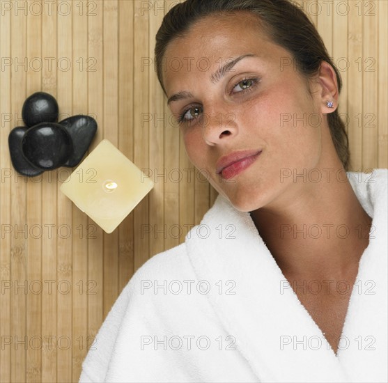 Woman in bathrobe laying next to stones and lit candle.