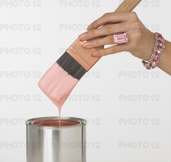 Woman's jeweled hand dipping paintbrush in paint can.