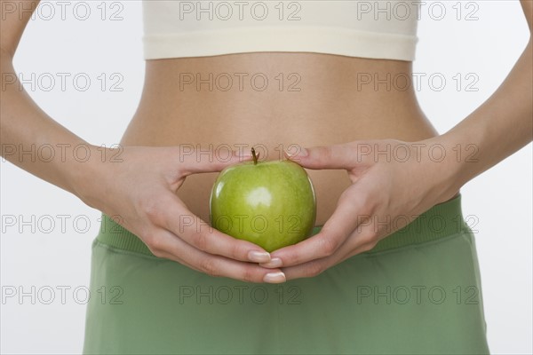 Studio shot of woman holding apple in front of belly.
