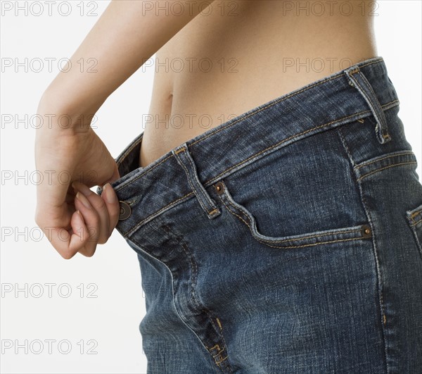 Close up of woman holding waist of pants away from stomach.