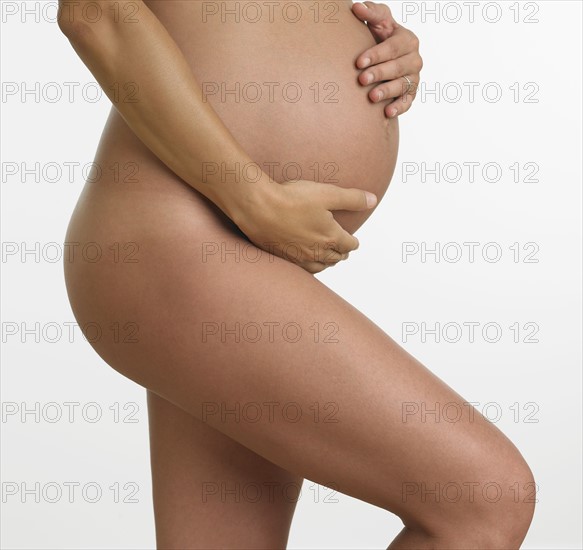 Studio shot of nude pregnant woman holding stomach.