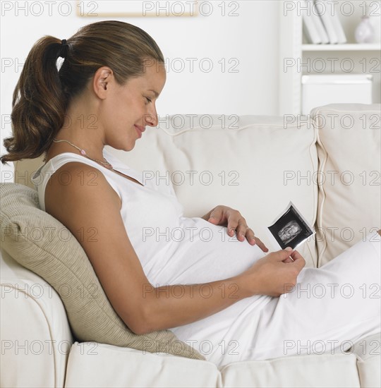 Pregnant woman on sofa smiling at ultrasound.