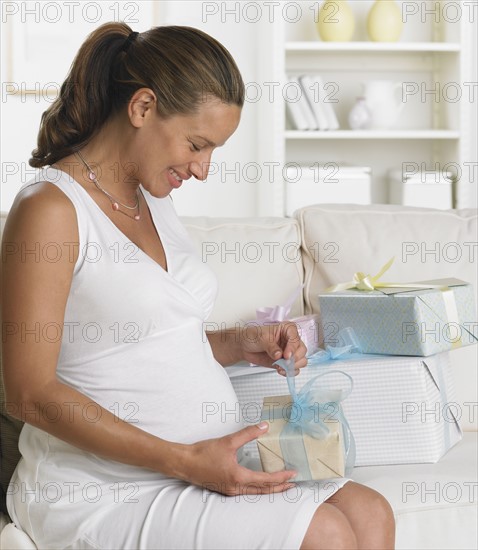 Pregnant woman on sofa opening gifts.