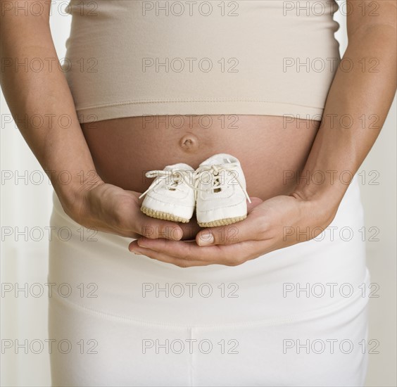 Pregnant woman holding baby shoes next to stomach.