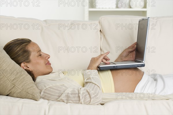 Pregnant woman on sofa using laptop.